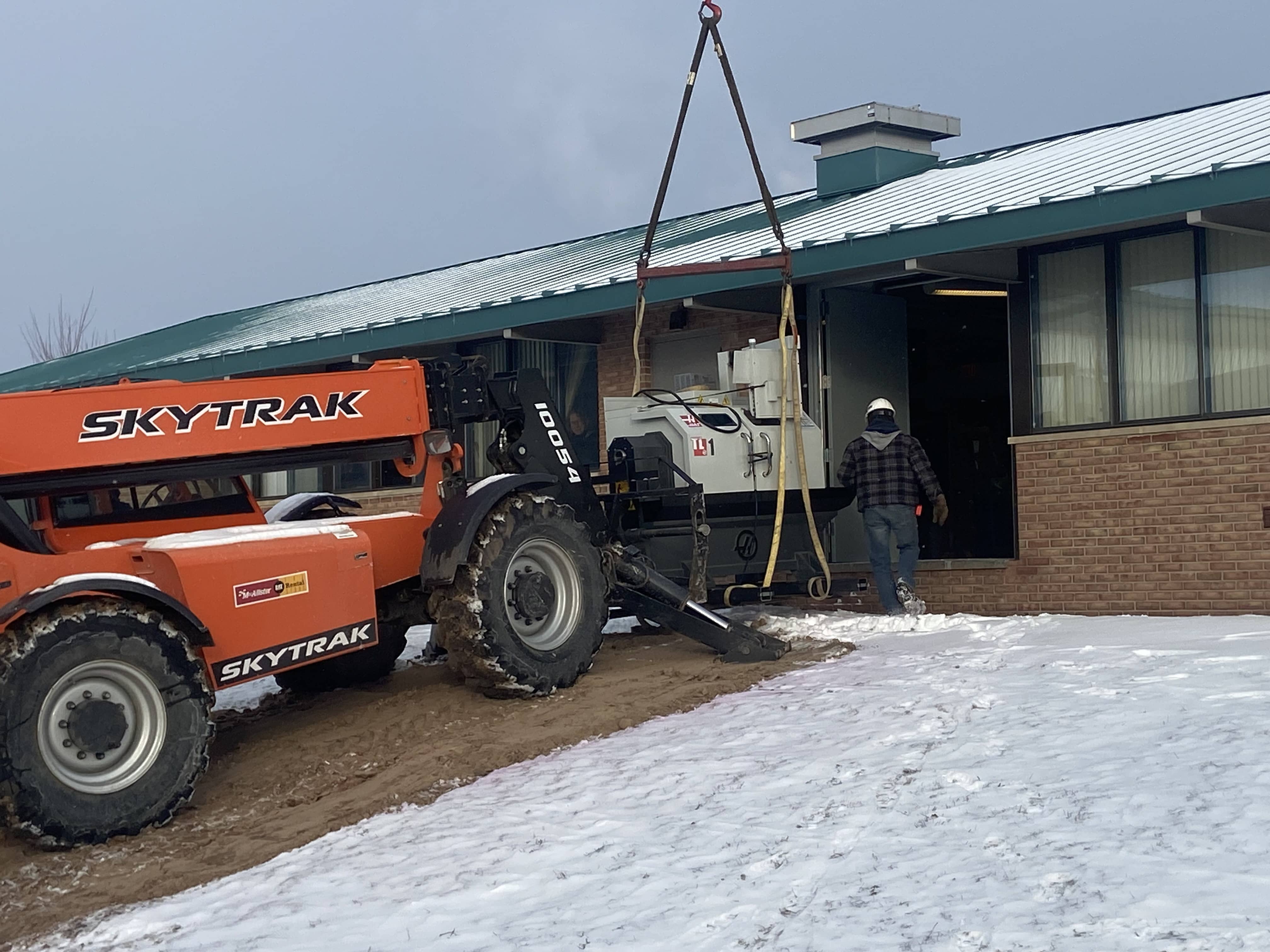 Skytrak forklift transporting CNC equipment into the Industrial Arts Institute building on a snowy day, showcasing North Central Michigan College's efforts to continue CNC training during construction