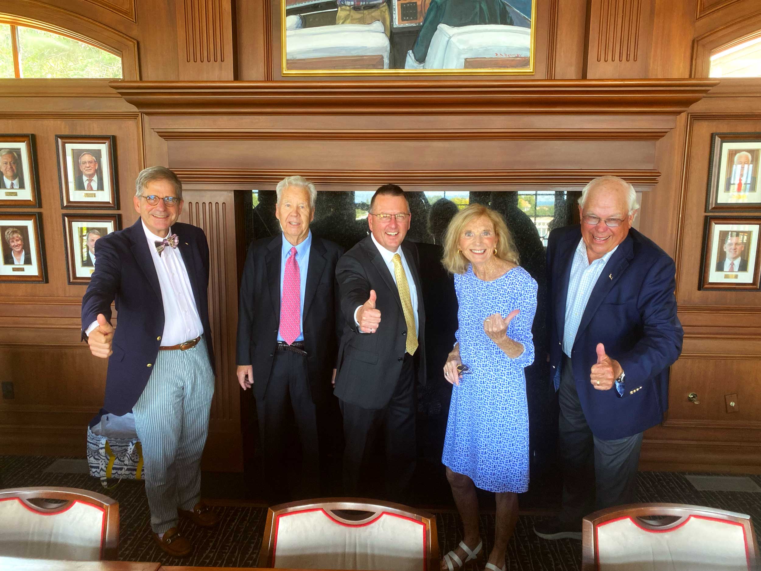 Five individuals standing, smiling with thumbs up