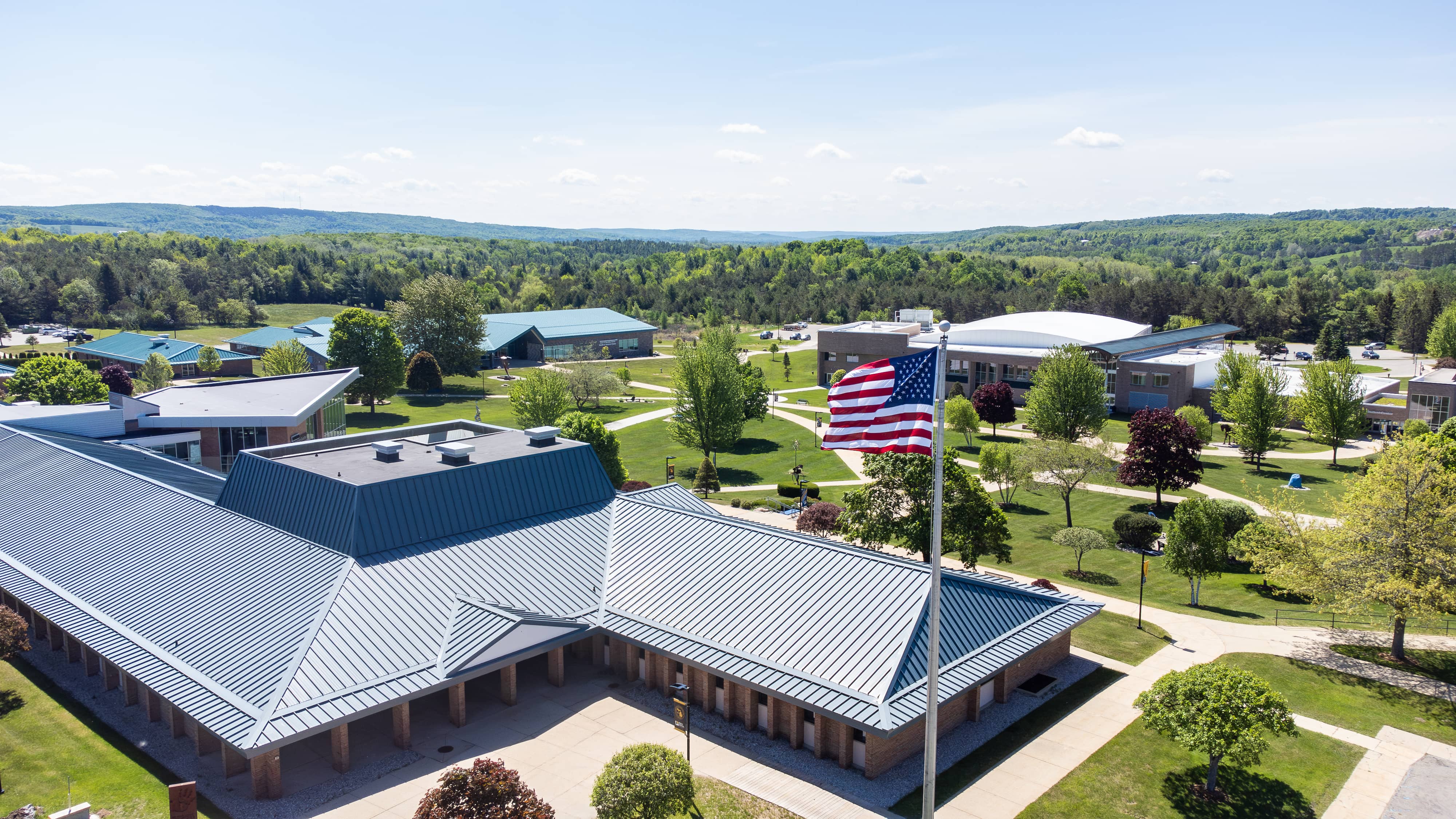 Aerial view of North Central Michigan College's Petoskey campus with academic buildings, green spaces and an American flag in the foreground