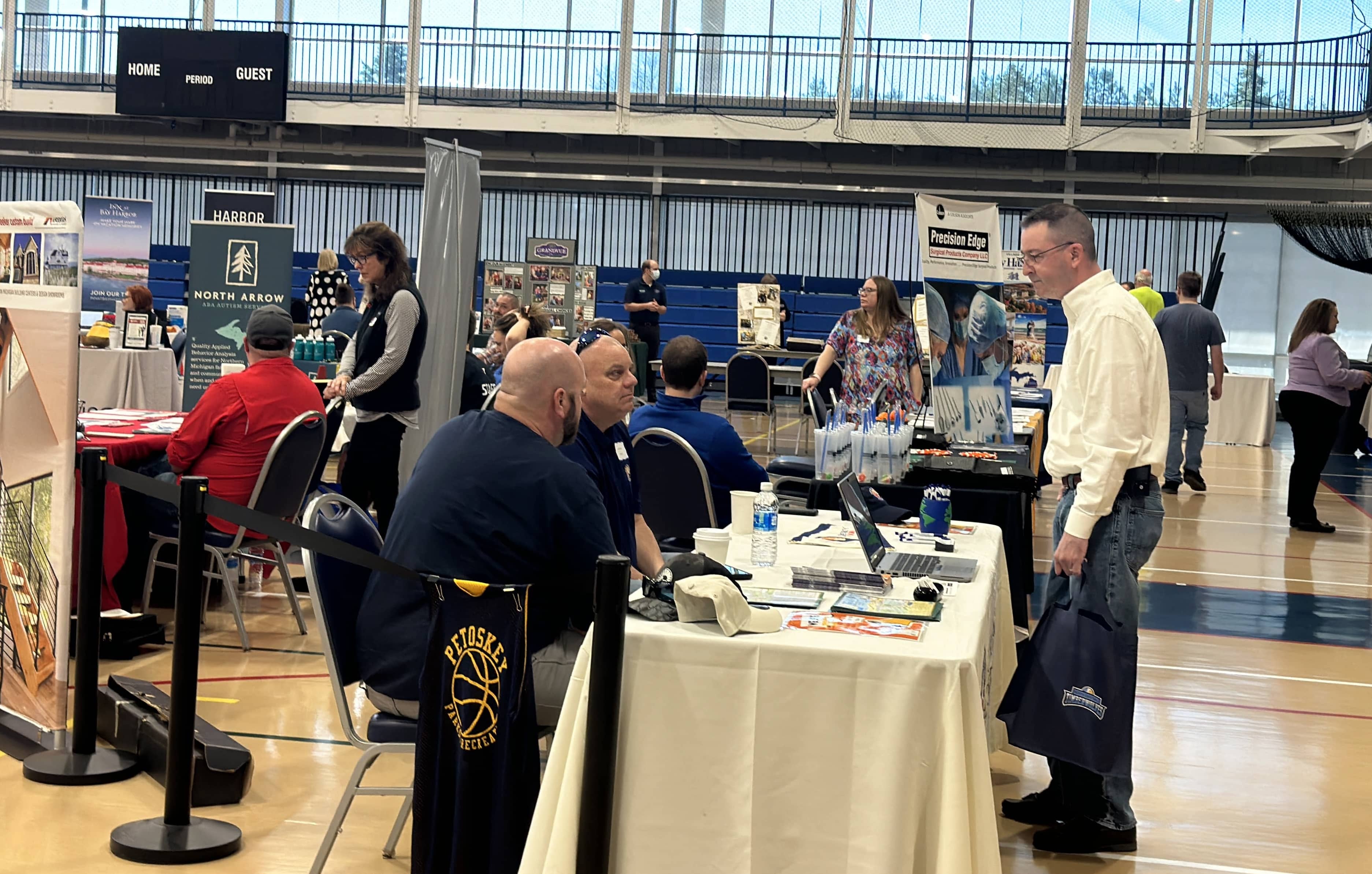 Employers and job seekers talk at booth tables during a job fair in the North Central Michigan College gymnasium