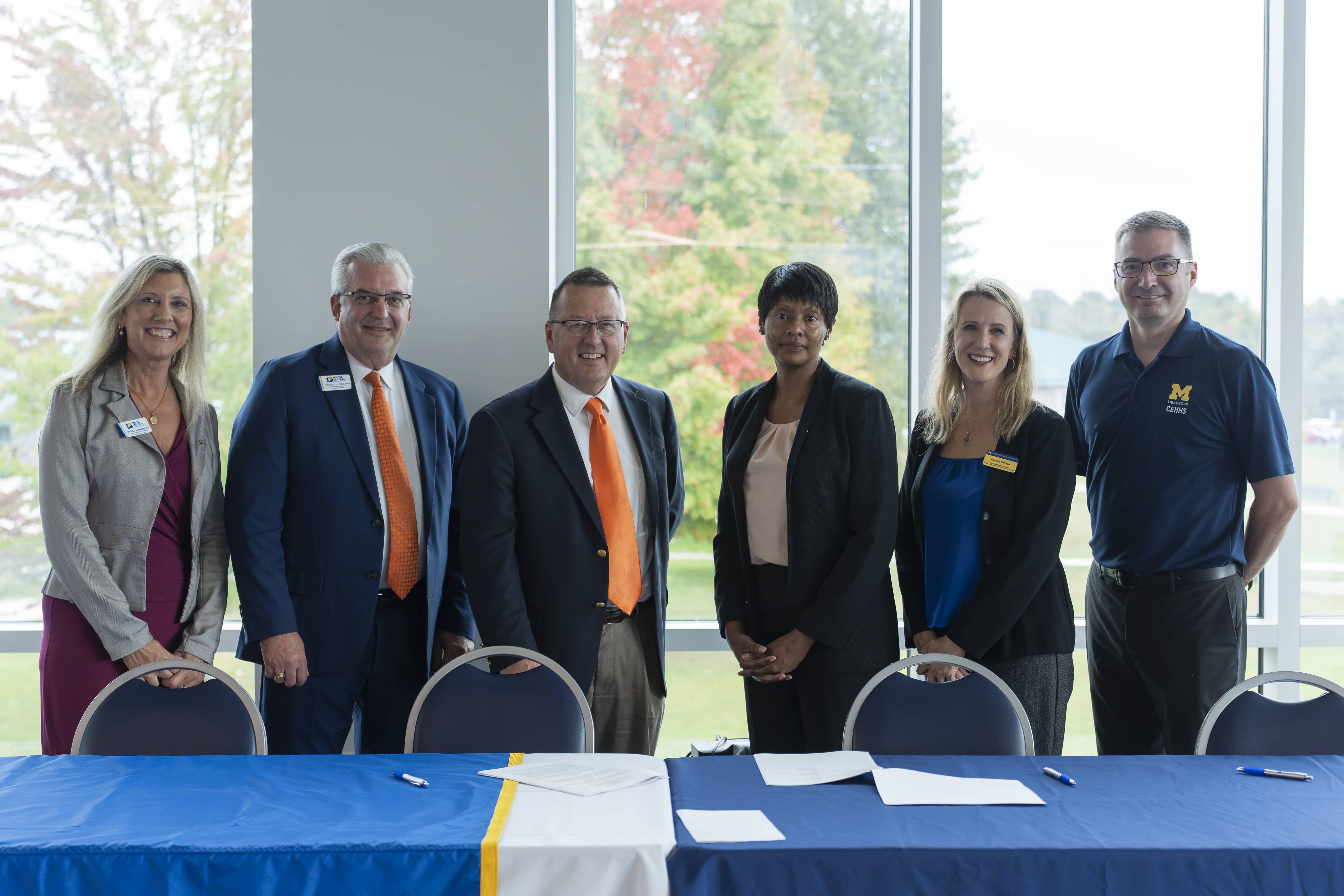 Six officials from North Central Michigan College and the University of Michigan-Dearborn stand behind a table at a teacher education partnership signing event.